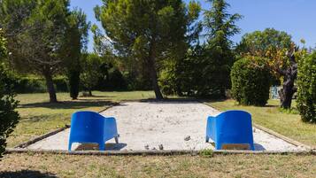 A courtyard with two blue chairs, a sandy area, and surrounding trees.