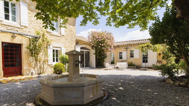 A courtyard with a fountain, stone walls, and a red door. - Chambre d'hôtes - B&B - Fleur de Coton (Lagnes)