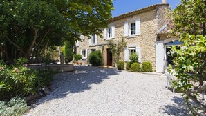 A stone building with a gravel driveway, surrounded by greenery and a clear blue sky. - Chambre d'hôtes - B&B - Fleur de Coton (Lagnes)