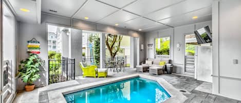 An indoor swimming pool area with a seating area, a potted plant, and a sign with directional arrows.
