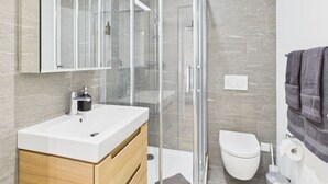 Un bagno moderno con cabina doccia in vetro, lavandino bianco e water.