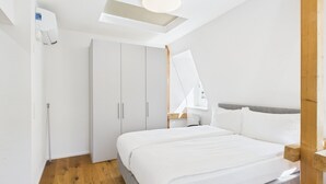 Una camera da letto moderna con un lucernario, un armadio bianco e un letto con biancheria da letto bianca.