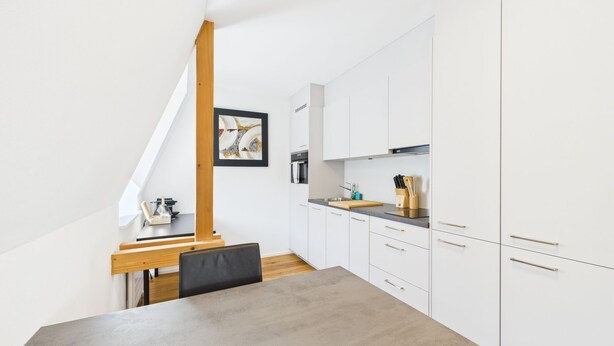 Una cucina moderna con mobili bianchi, un tavolo da pranzo in legno e una sedia nera.