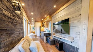 A modern living room with a stone wall, wooden ceiling, and a large TV mounted on a white wooden wall.