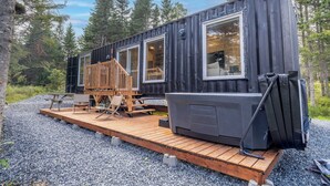 A modern cabin with large windows, a wooden deck, and a hot tub.