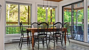 Comedor con mesa y sillas de madera, ventanas amplias y vistas a zonas verdes.