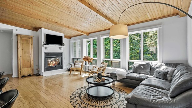 Una sala de estar moderna con chimenea, techo de madera, ventanas amplias y un sofá gris.