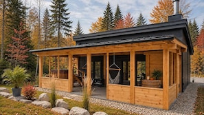 En stuga byggd av trä med en inglasad veranda, en hängstol och en öppen spis.
