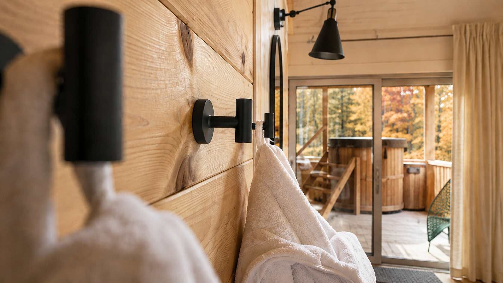 A wooden interior with a towel hanging on a wall-mounted hook, a black lamp, and a view of an outdoor deck with a table and chairs.