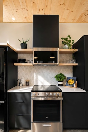A modern kitchen with a stainless steel stove, black cabinetry, and wooden ceiling.