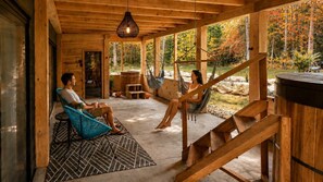 Eine Holzhütte mit zwei Personen, die auf Stühlen sitzen, einer Hängematte und einer Holztreppe.
