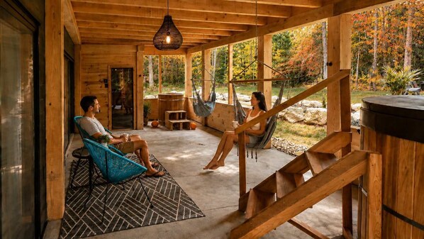 A wooden cabin with two people sitting on chairs, a hammock, and a wooden staircase.