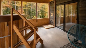 Un intérieur en bois avec un escalier, une porte vitrée donnant sur l’extérieur et une chaise.