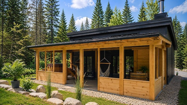 A wooden cabin with a covered porch, a fireplace, and a view of surrounding trees.