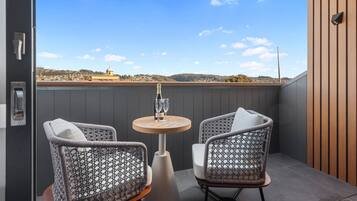 A balcony with wicker chairs, a small round table, and a view of a distant town.