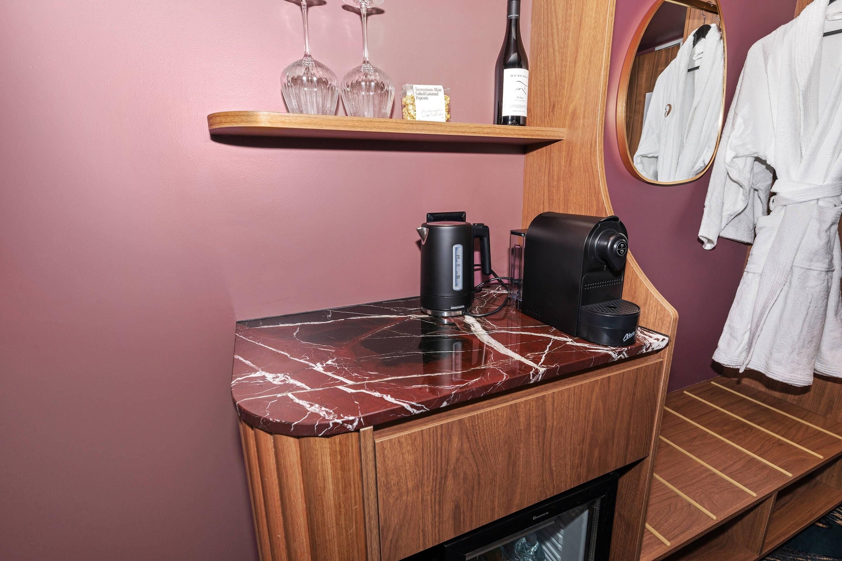 Een badkamer met een houten wastafelmeubel, een marmeren aanrecht, een koffiezetapparaat, een fles wijn en een badjas die aan een rek hangt.