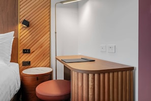A compact room with a bed, a small wooden table with a tablet, a round wooden stool, and a wall-mounted lamp. - George Hotel Launceston, An Ascend Collection Hotel (Launceston)