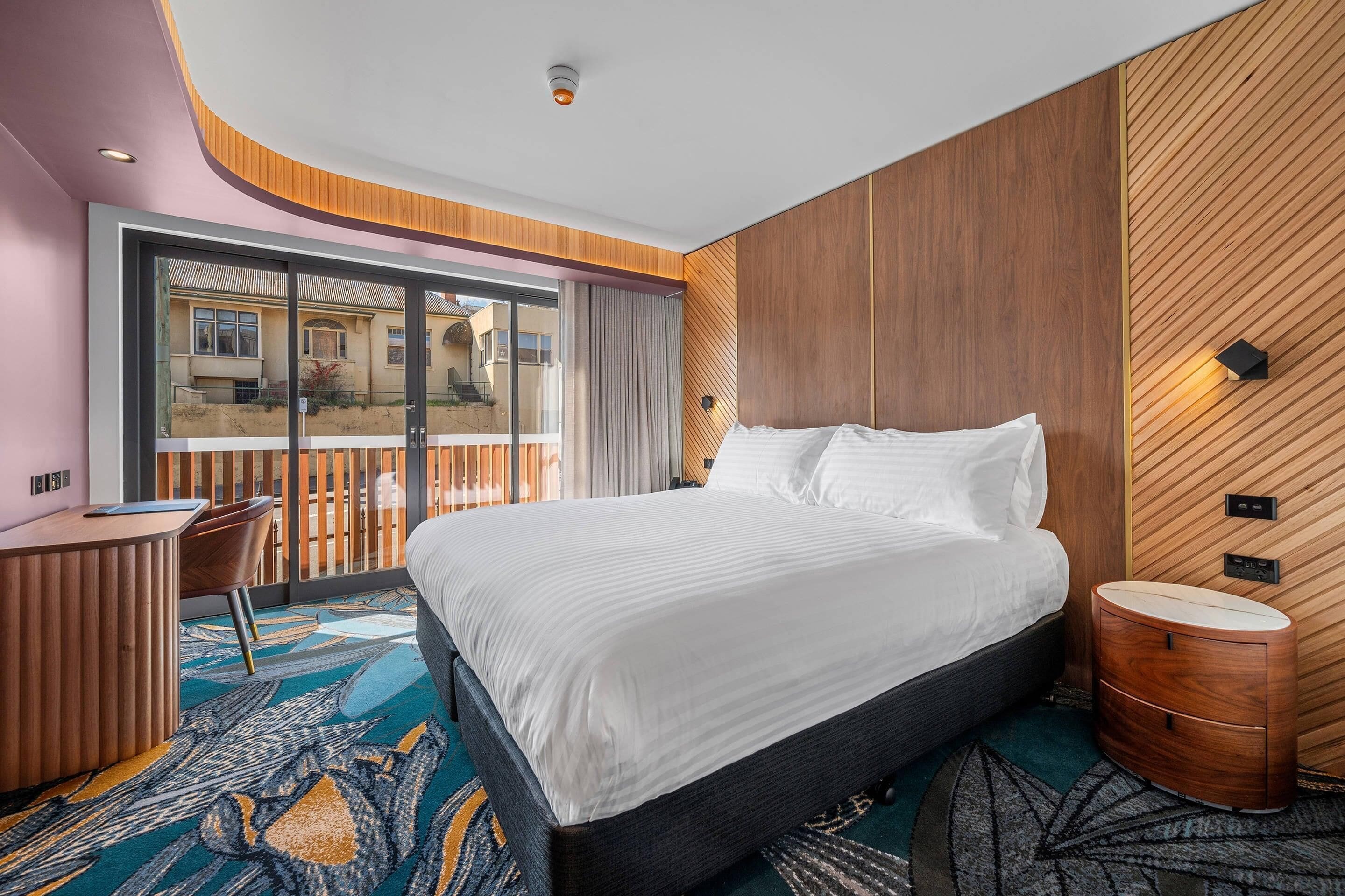 A modern hotel room with a large bed, a desk, and a view of the outside.