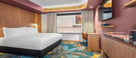 A hotel room with a bed, desk, chair, and a large window.
