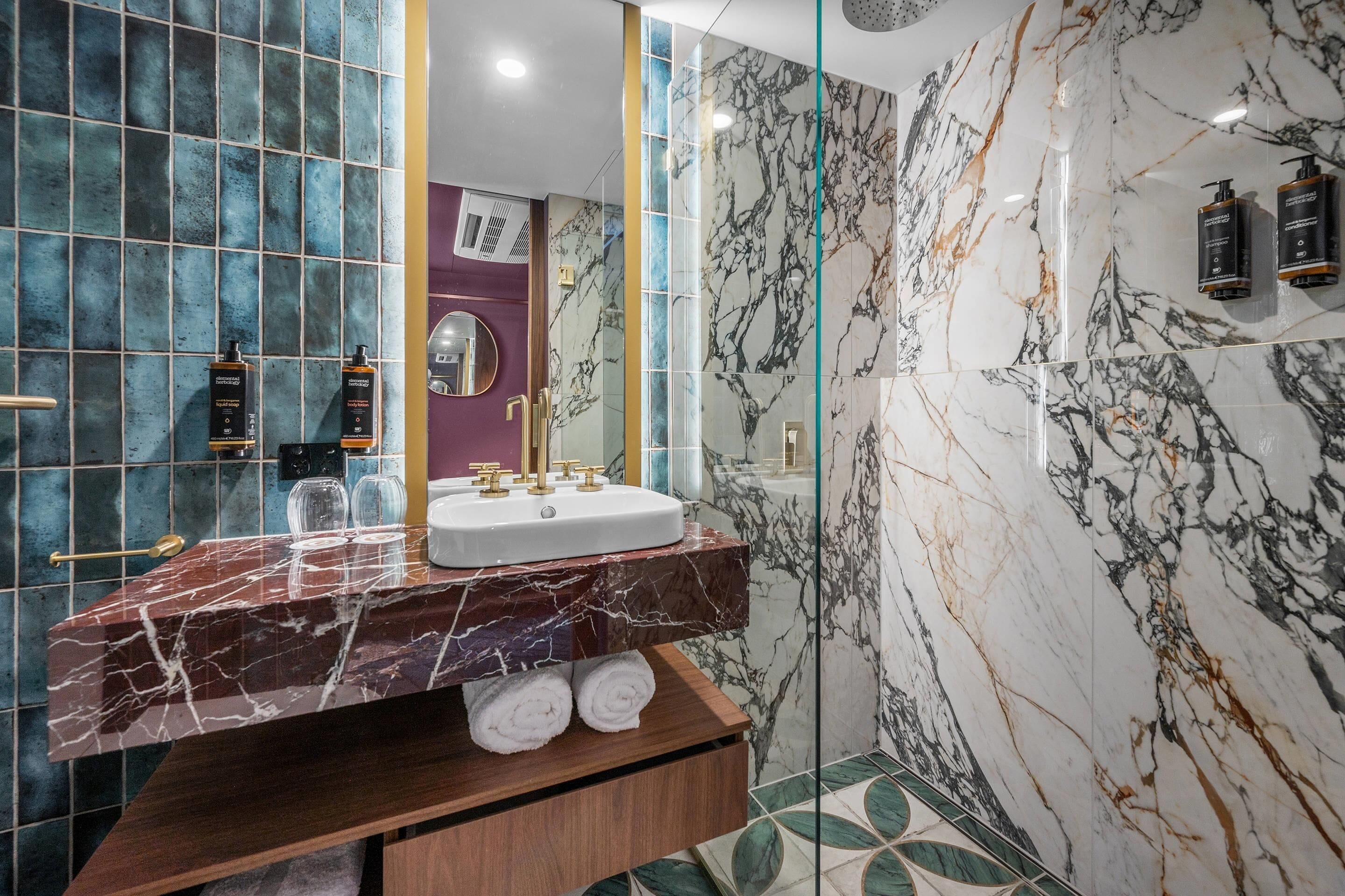 A modern bathroom with a marble sink, glass shower enclosure, and a vanity with towels.