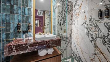A modern bathroom with a marble sink, glass shower enclosure, and a vanity with towels.