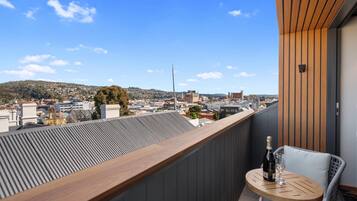 A balcony with a view of a cityscape, a wooden table with a bottle and glass, and a white chair.