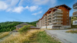A multi-story hotel with balconies, a road in front, and a forested hillside in the background. - Charming Apart for 6 near the Ski Slopes (Allos)