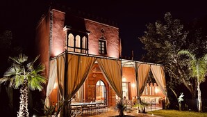 A large, historic building with a courtyard, featuring a dining area with tables and chairs, surrounded by palm trees and a well-lit walkway. - Magnificent Villa-Riad with private garden, large Jacuzzi in a private estate (Marrakech)