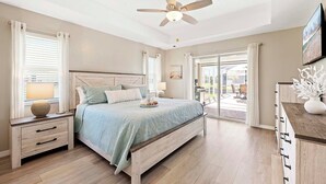 Een slaapkamer met een bed, nachtkastjes, een plafondventilator en uitzicht op de omgeving via een schuifdeur.
