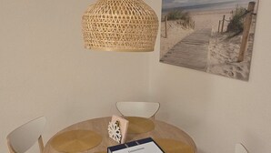 A round wooden dining table with four chairs, a woven pendant light, and a framed beach painting on the wall. - Beautiful vacation apartment in Timmendorfer Strand (Timmendorfer Strand)