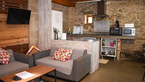 Un espacio de sala de estar acogedor con un sofá y una mesita de centro, una kitchenette con microondas y tostadora, y una pared de piedra.