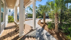 A covered outdoor area with wooden flooring, white columns, and a view of a residential street with palm trees and houses. - Steps to Seacrest! Private Pool, Bikes, 4 KING Bedrooms! Beach Tram! (Santa Rosa Beach)
