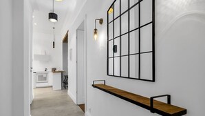 A hallway with a wooden shelf, a grid-patterned wall decoration, and pendant lighting. - Muranów Apt - 49m2, City View - By Rentujemy (Warszawa)