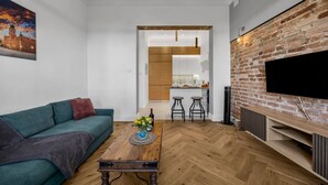 A modern living room with a green sofa, a wooden coffee table, and a brick wall with a TV. - Muranów Apt - 49m2, City View - By Rentujemy (Warszawa)