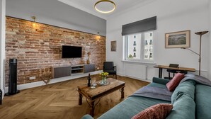 A living room with a brick wall, a flat-screen TV, a wooden coffee table, and a green sofa. - Muranów Apt - 49m2, City View - By Rentujemy (Warszawa)
