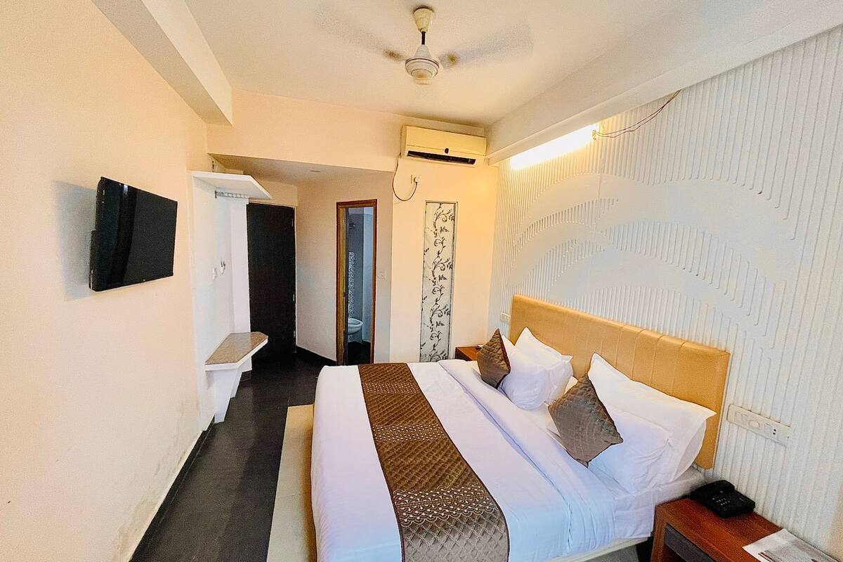 A hotel room with a bed, bedside table, and a flat-screen TV mounted on the wall.