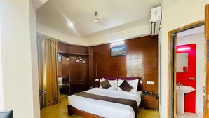 Une chambre d’hôtel avec un grand lit, une tête de lit en bois, une armoire, une table de chevet, une commode, un miroir et une porte rouge donnant accès à la salle de bain.
