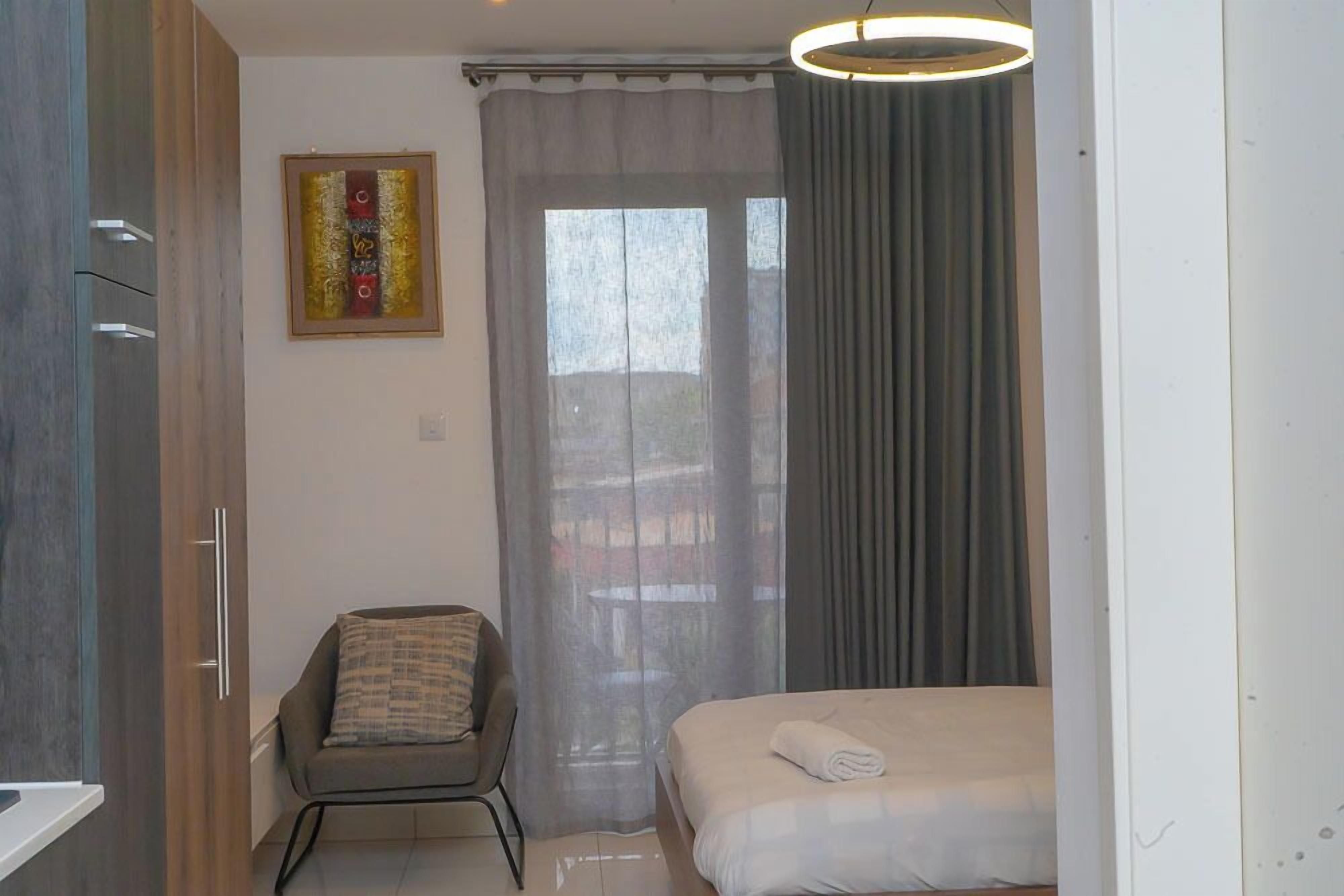 Un dormitorio con cama, una silla, un ventanal con cortinas y un cuadro en la pared.