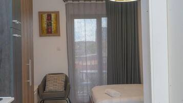 Un dormitorio con cama, una silla, un ventanal con cortinas y un cuadro en la pared.