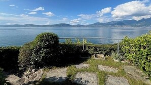Blick auf einen See mit blauem Himmel, fernen Bergen und einem Metallgeländer.
