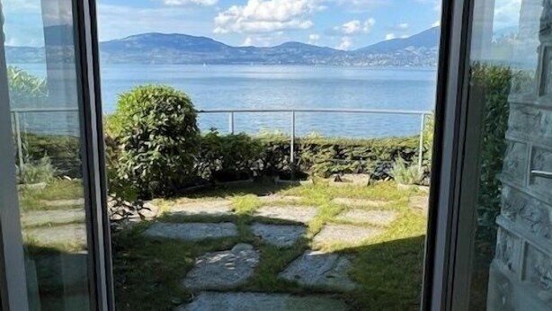 Ein Zimmer mit Glastür, das auf einen Balkon mit Blick auf einen See und Berge führt.