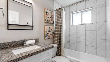 A bathroom with a granite countertop sink, a toilet, a bathtub, and a shower curtain.