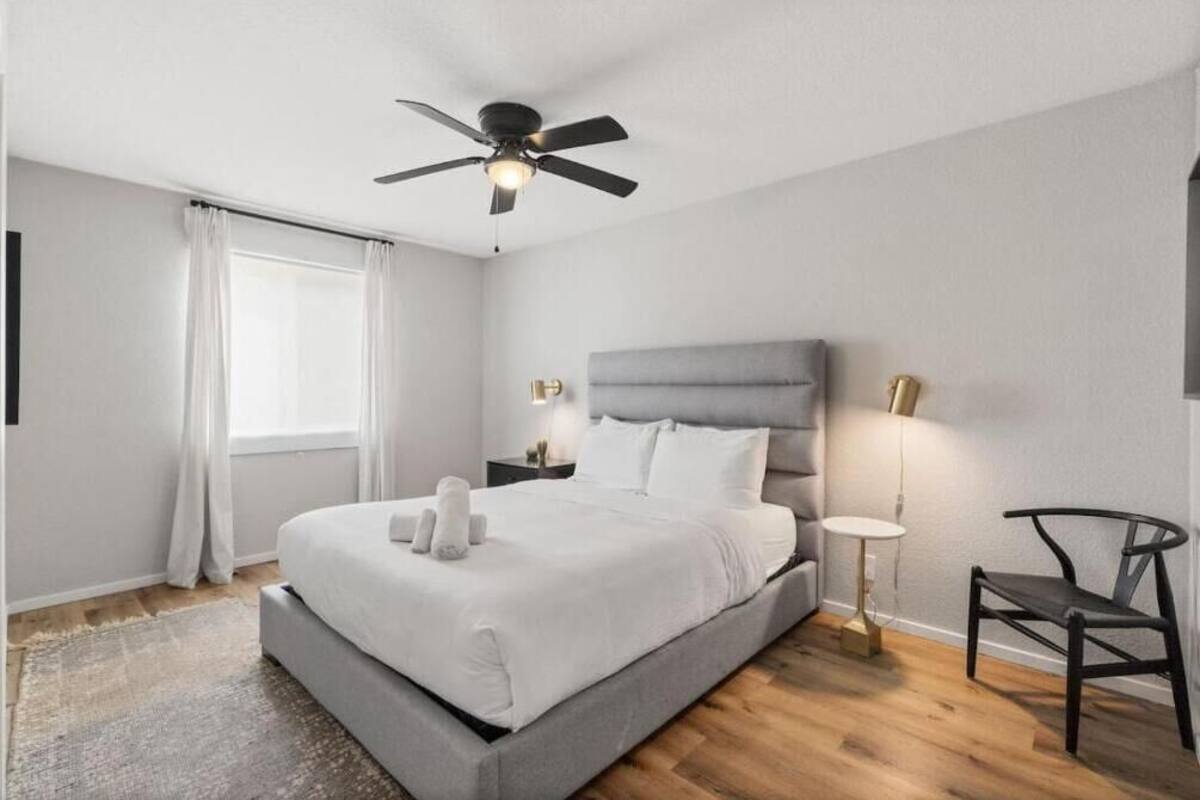 Un dormitorio moderno con una cama grande, un ventilador de techo, una mesita de noche con lámpara y una silla.