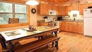 A wooden kitchen with a large dining table, wooden cabinets, and a window with a view of trees.