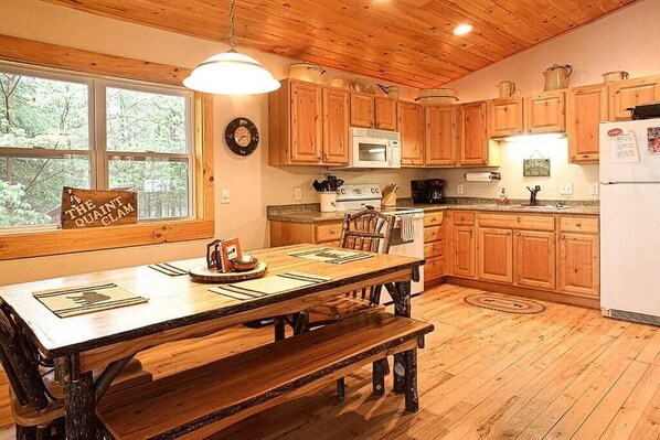 A wooden kitchen with a large dining table, wooden cabinets, and a window with a view of trees.