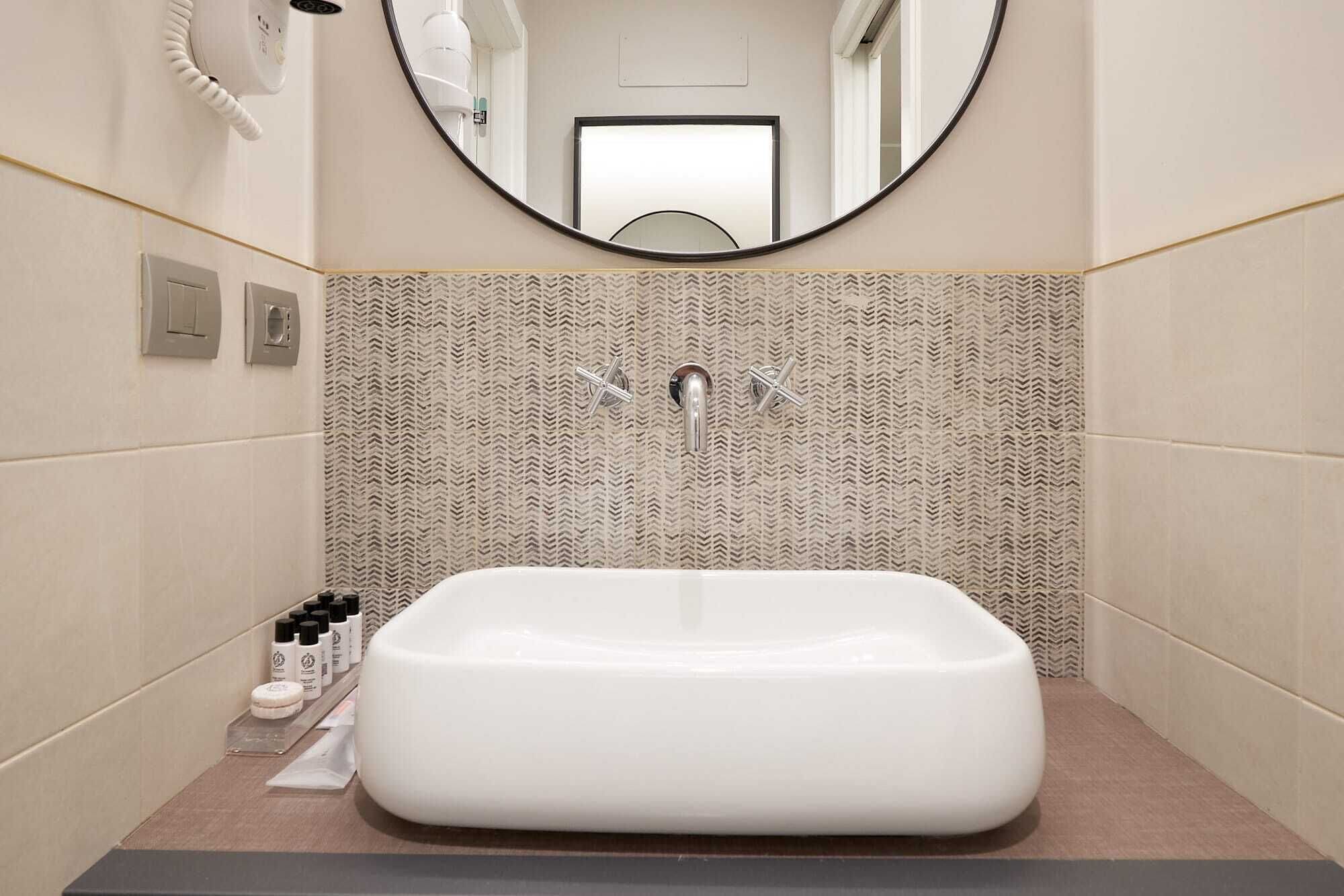 A modern bathroom with a large rectangular sink, a wall-mounted mirror, and a patterned tile backsplash.