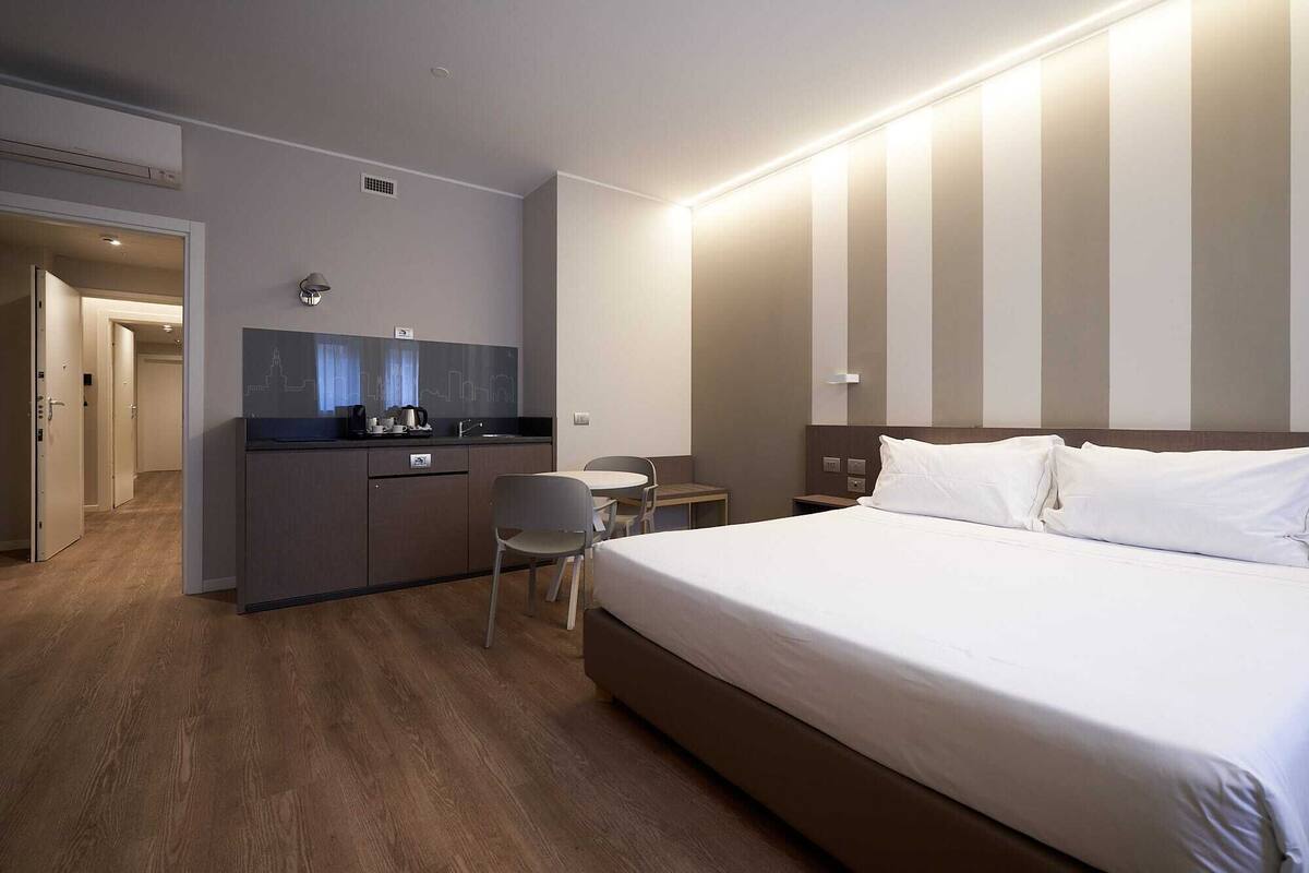 Habitación de hotel con cama, escritorio, silla, una mesita y kitchenette.