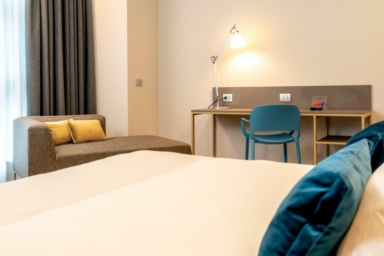 A hotel room with a bed, a desk, a chair, and a sofa.