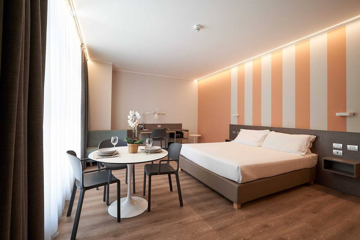 Una habitación de hotel moderna con una cama, una mesa de comedor con sillas y un pequeño escritorio.