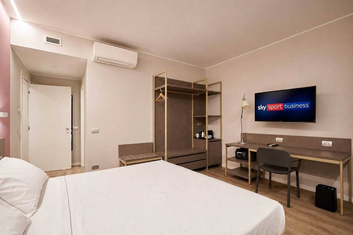 Una habitación de hotel con cama, escritorio, silla, televisor y armario.